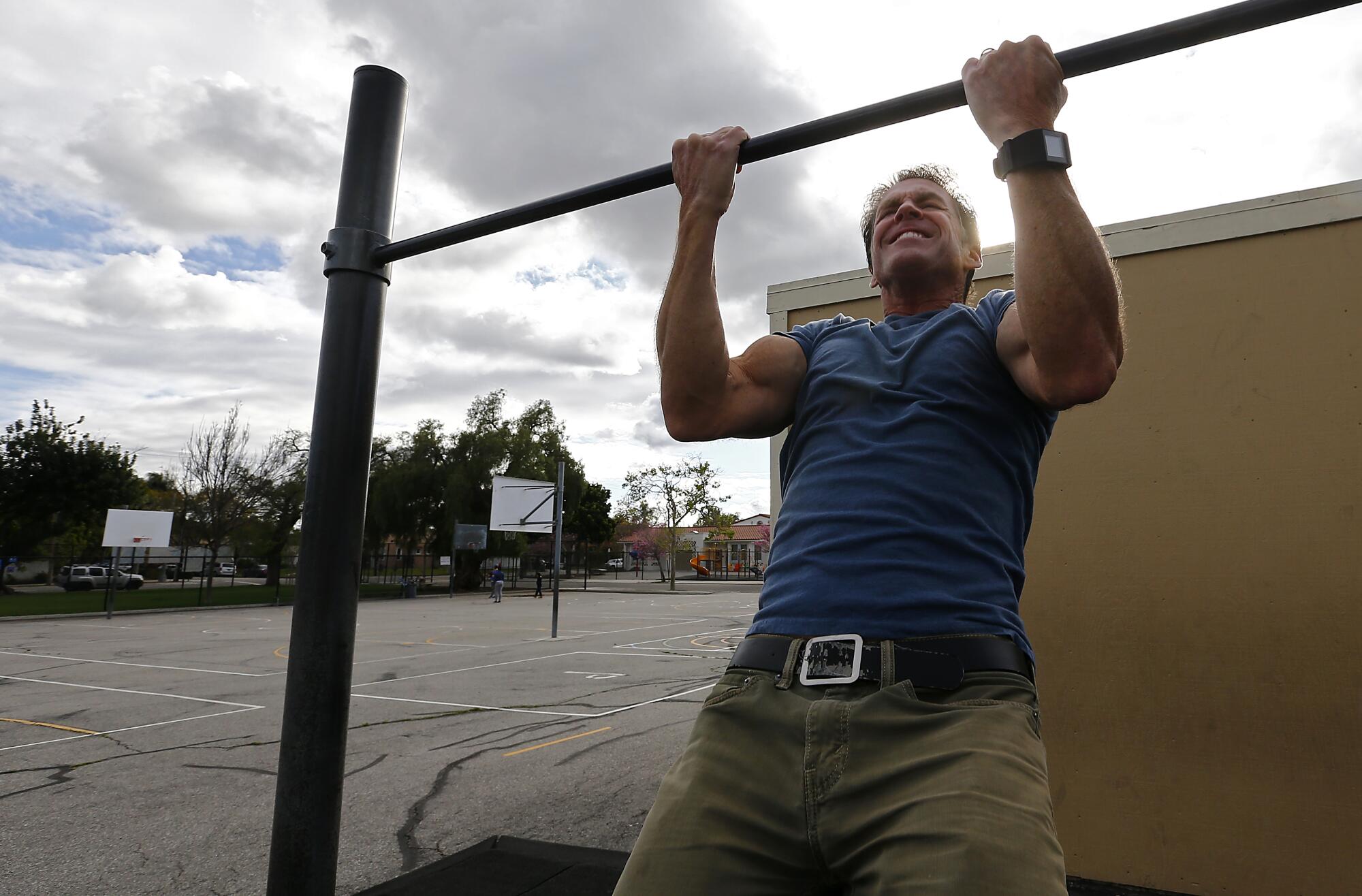 Mike Lynn grimaces as he does a pull-up on playground exercise equipment.