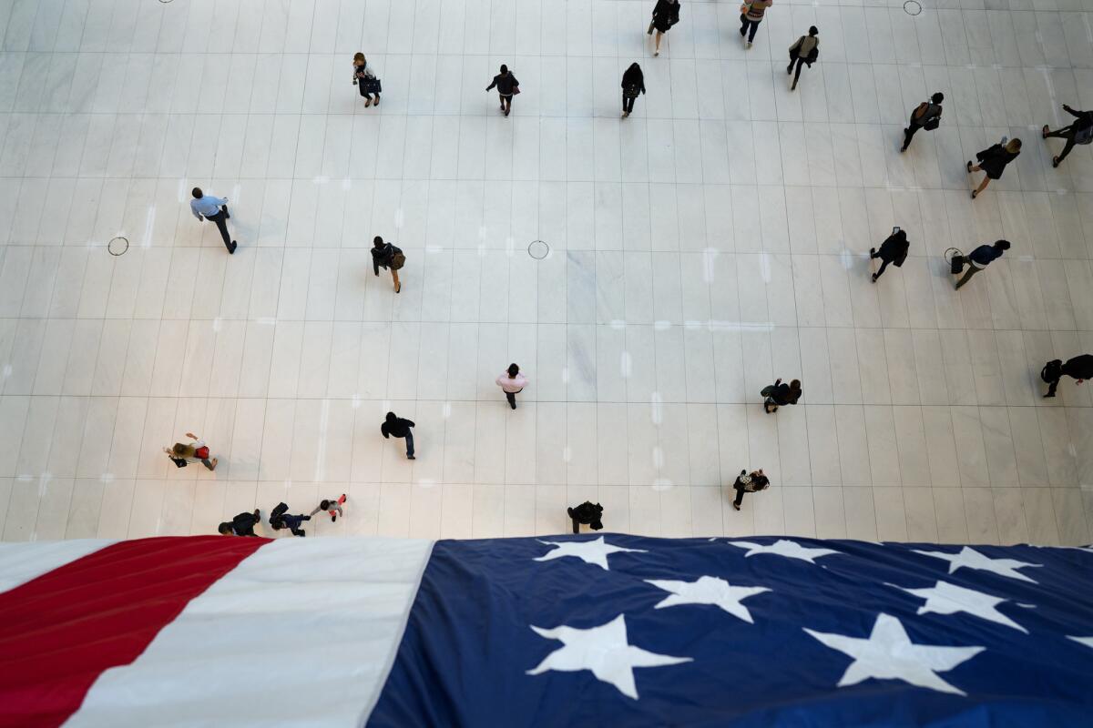 People walk under an American flag inside the Oculus, part of the World Trade Center transportation hub, on the anniversary of 9/11 terrorist attacks in New York on Tuesday, Sept. 11, 2018. (AP Photo/Craig Ruttle)