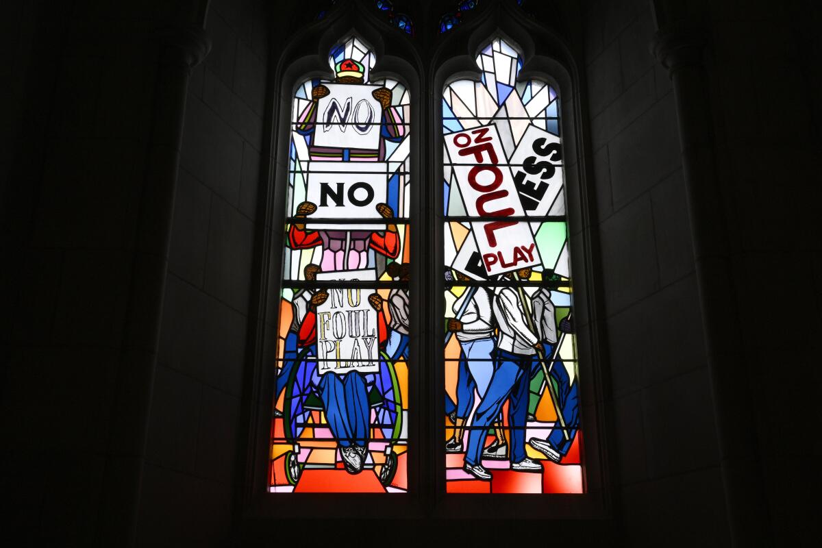 Light shines through new stained-glass windows with images of people holding signs saying No Foul Play.