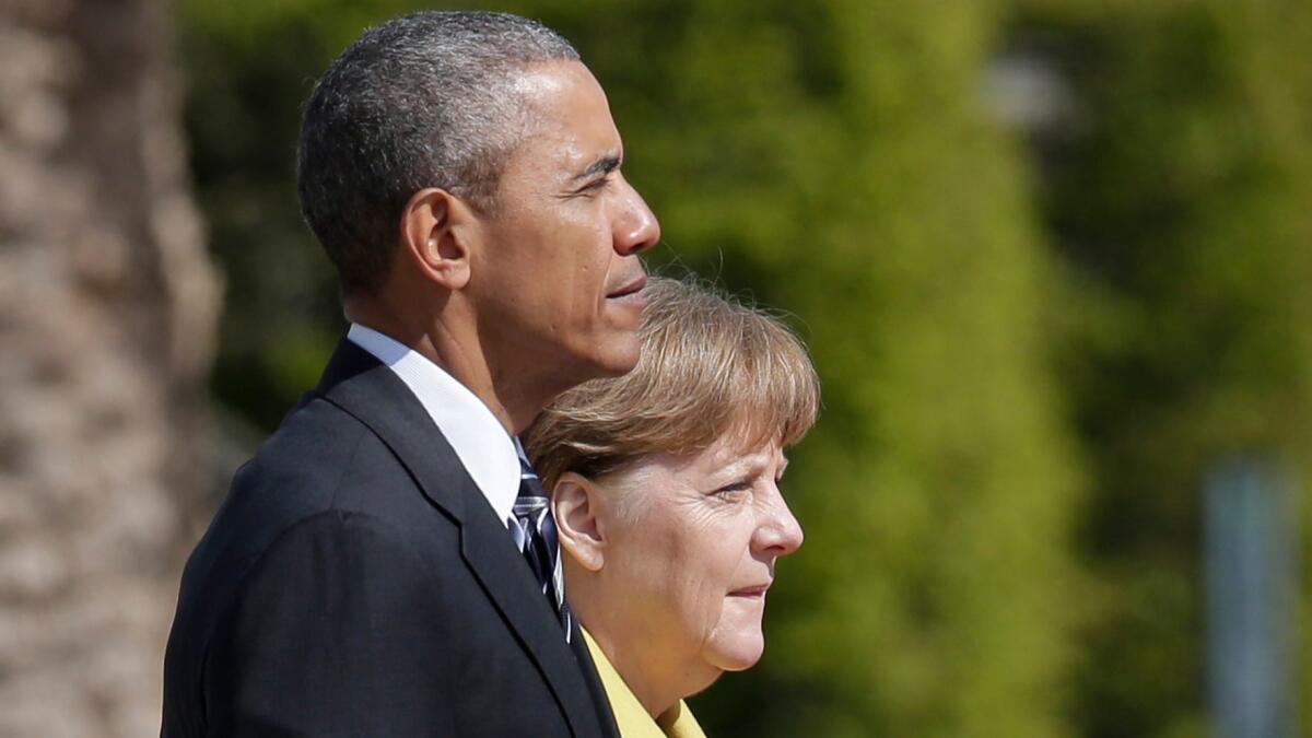 German Chancellor Angela Merkel and then-President Obama listen to the national anthems during a welcoming ceremony at Herrenhausen Palace in Hannover, Germany, on April 24, 2016.