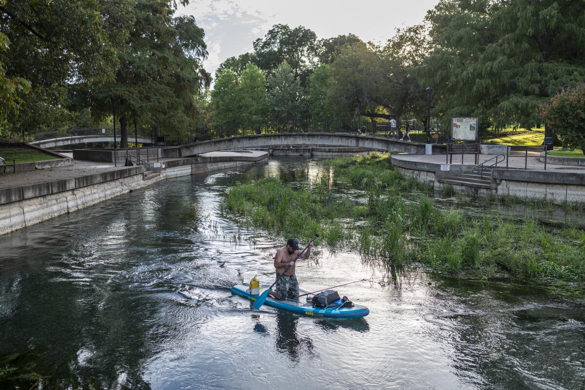 A person rows a paddleboard through the San Marcos river in San Marcos, Texas.