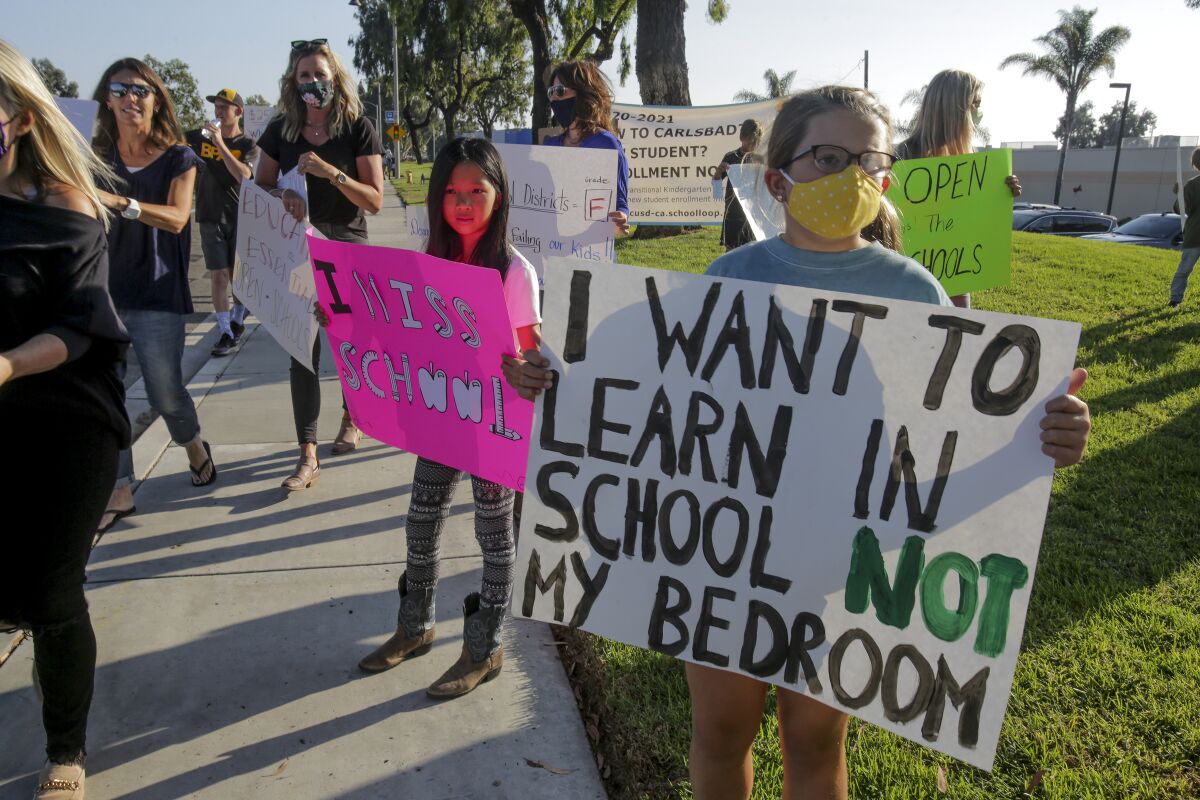 Morgan Yang, 9, center, and Lucy Riddle, 10, display signs urging officials to reopen schools in Carlsbad in September.
