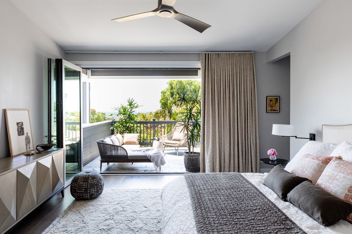 A serene bedroom in a beach home includes soft textures in bedding, open access to a deck and views, and collected art.