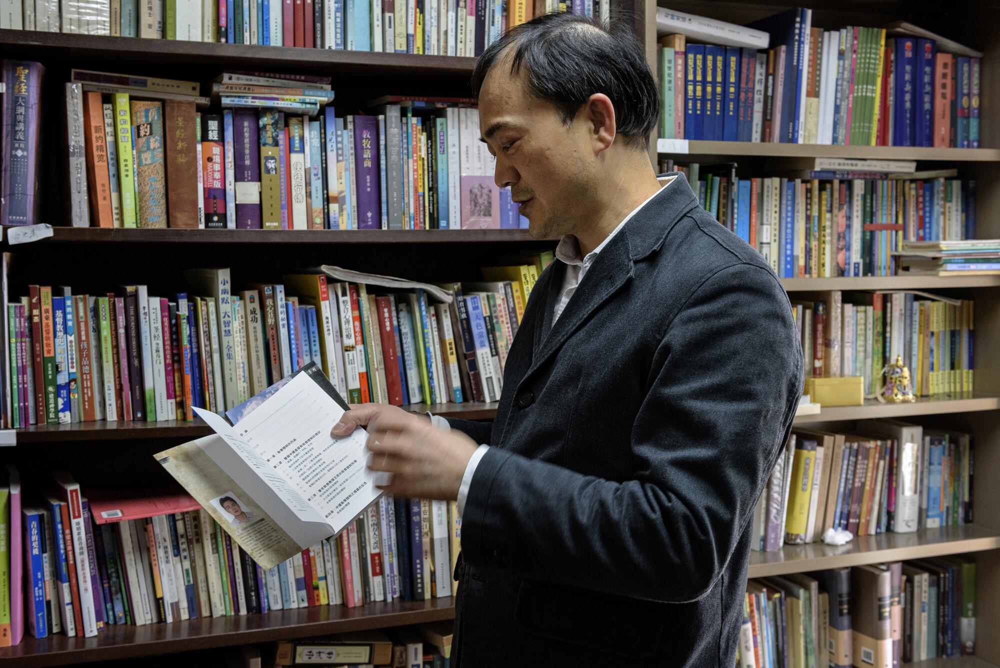 A man flips through a book in front of a bookshelf filled with books