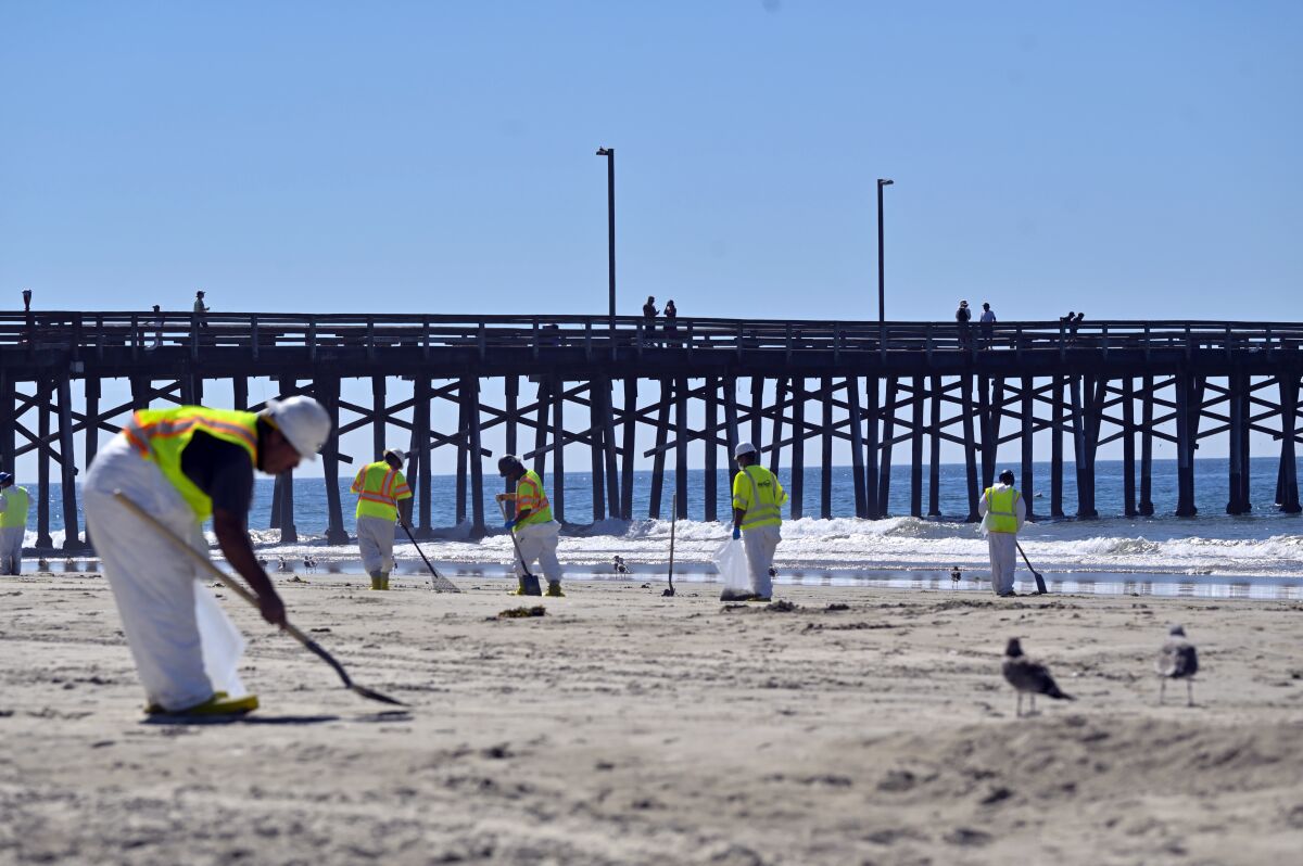 Workers clean oil from the sand, south of the pier, in Newport Beach, Calif., Tuesday, Oct. 5, 2021. A leak in an oil pipeline caused a spill off the coast of Southern California, sending about 126,000 gallons of oil into the ocean, some ending up on beaches in Orange County. (Jeff Gritchen/The Orange County Register via AP)