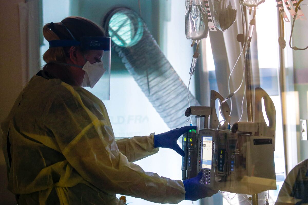 A nurse checks on IV pumps attached to a COVID-19 patient.