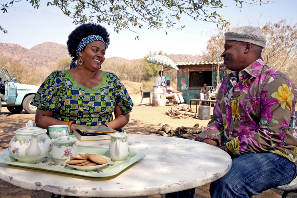 A woman and a man sit at an outdoor table with a tray of afternoon tea and cookies.