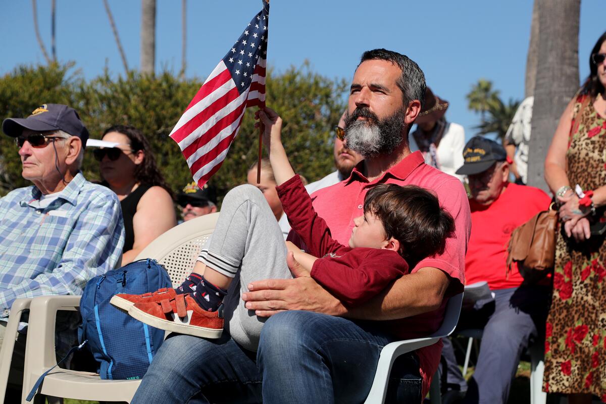 George Carlton, 4, holds up the American flag as he lays in the lap of his father, Slade, during a Veterans Day ceremony.