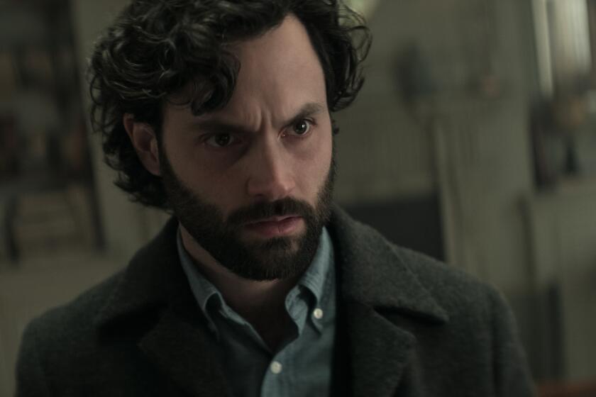 A close-up shot of a man with curly brown hair and a beard staring intensely