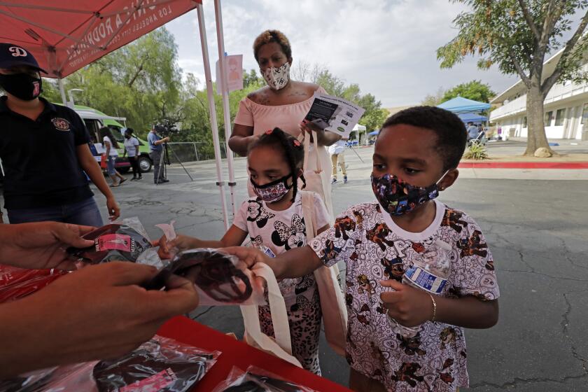 SYLMAR, CA - AUGUST 17: Jazzmin (cq) Turman (cq) waits on her children Khanukkah, 4, (cq, left) and Shalom, 3, picking up school supplies and masks during a back-to-school fair at the Vagabond Inn in Sylmar on Monday, Aug. 17, 2020. The event, on the first day of school, was a partnership between Councilwoman Monica Rodriguez and L.A. Family Housing providing students with backpacks full of school supplies and other essential items for the family. The families participating are those facing economic hardship because of the pandemic. (Myung J. Chun / Los Angeles Times)