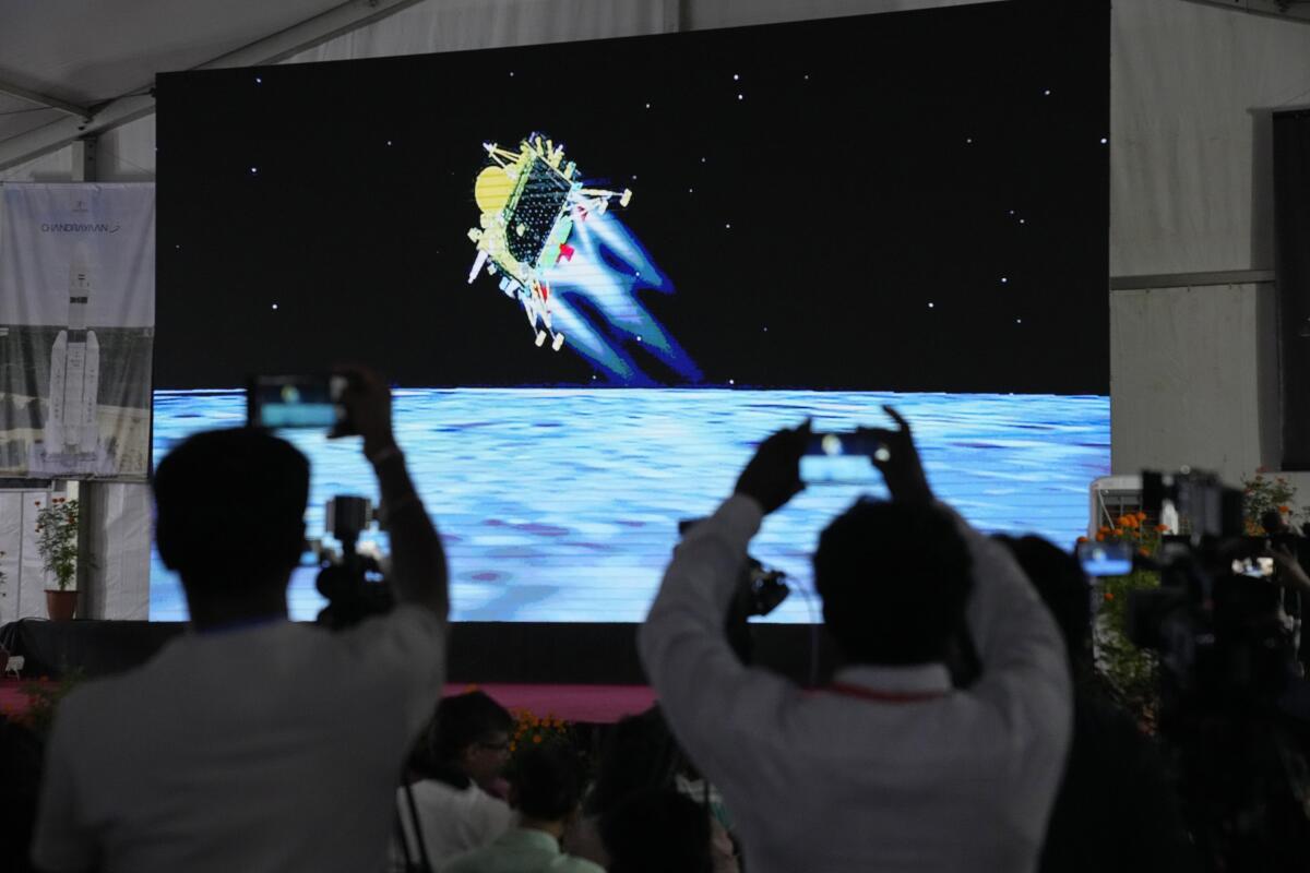 People hold up cellphones in front of a screen showing a lunar landing.