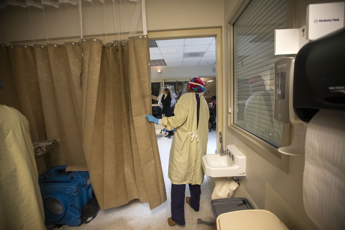 A doctor peers out from behind an emergency room curtain.