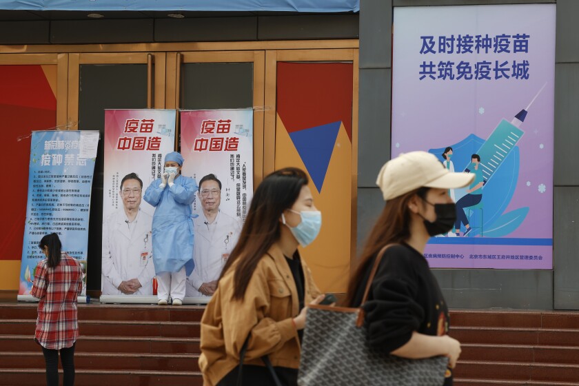 A medical worker stands near billboards portraying renowned Chinese Dr. Zhong Nanshan with the words "Vaccine China Made" at a vaccination site in Beijing on Friday, April 9, 2021. China's success at controlling the coronavirus outbreak has resulted in a population that has seemed almost reluctant to get vaccinated. Now, it is accelerating its inoculation campaign by offering incentives — free eggs, store coupons and discounts on groceries and merchandise — to those getting a shot. (AP Photo/Ng Han Guan)