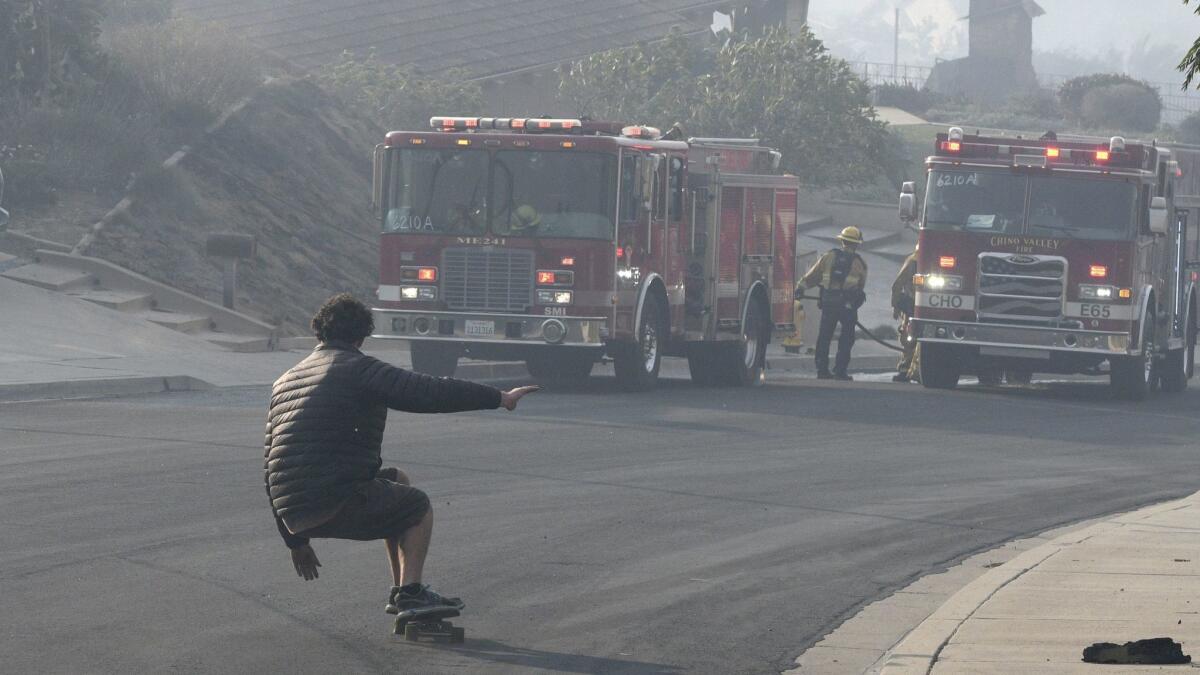 Tyler Mobley skateboards by firefighters in the Clear Point neighborhood in Ventura. Mobley's house survived.