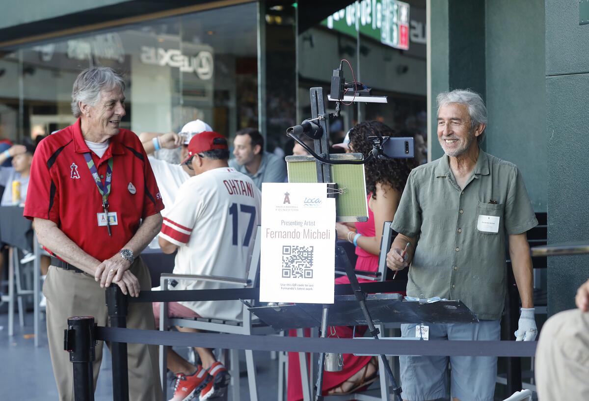 Artist Fernando Micheli, right, is joined Wednesday by an Angels staff member during a live demonstration at Angel Stadium.