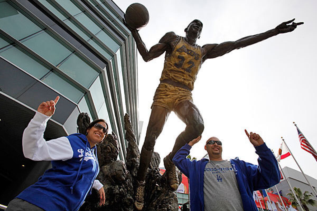Urber Dodgers fans, Kathleen Enriquez and Mike Enriquez pose alongside the Magic Johnson statue outside Staples Stadium.