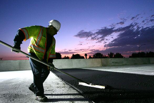 A worker sweeps the new asphalt surface on a portion of the 710 Freeway in Long Beach. The I-710 Long Life Pavement Project, as Caltrans calls it, began in 2001, is scheduled for completion in the next five years and is a projected to cost $650 million.