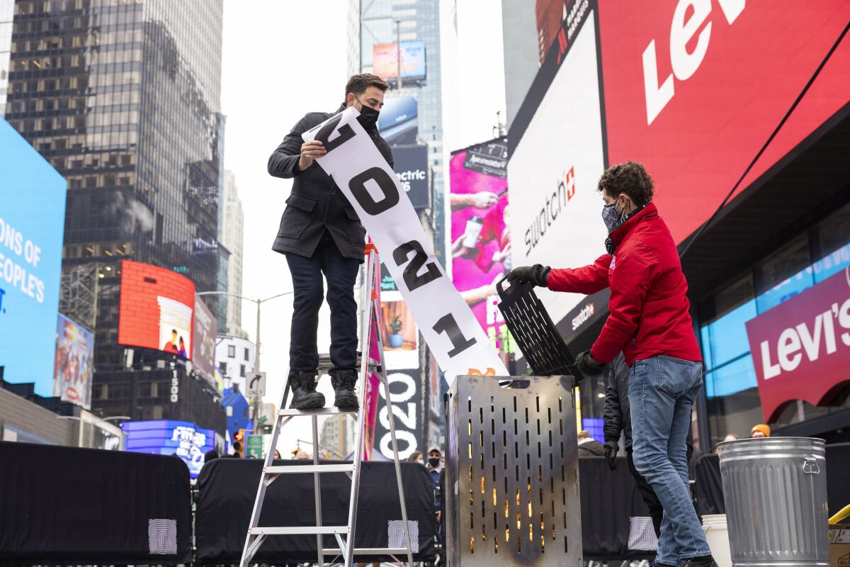 Two men putting a "2021" banner into a burning bin