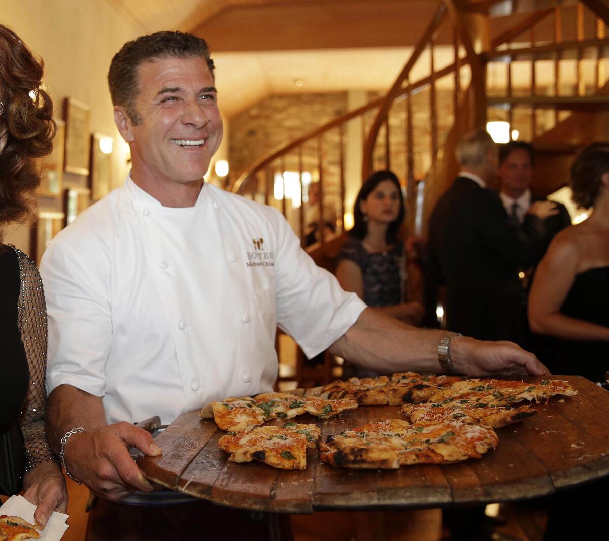 A smiling man holds a rustic wooden platter with slices of pizza.