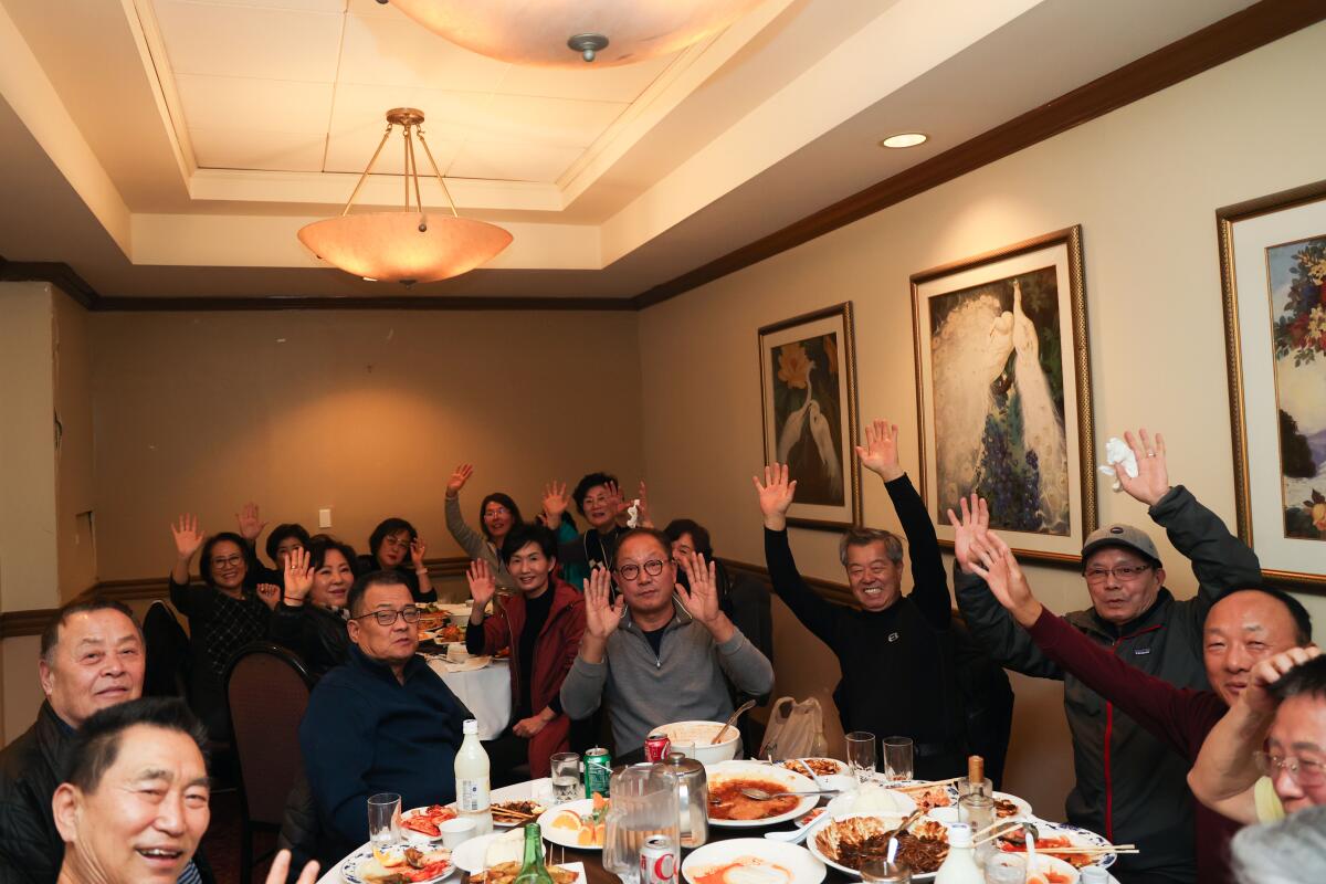 A crowded restaurant dining room filled with happy-looking people, many raising both hands