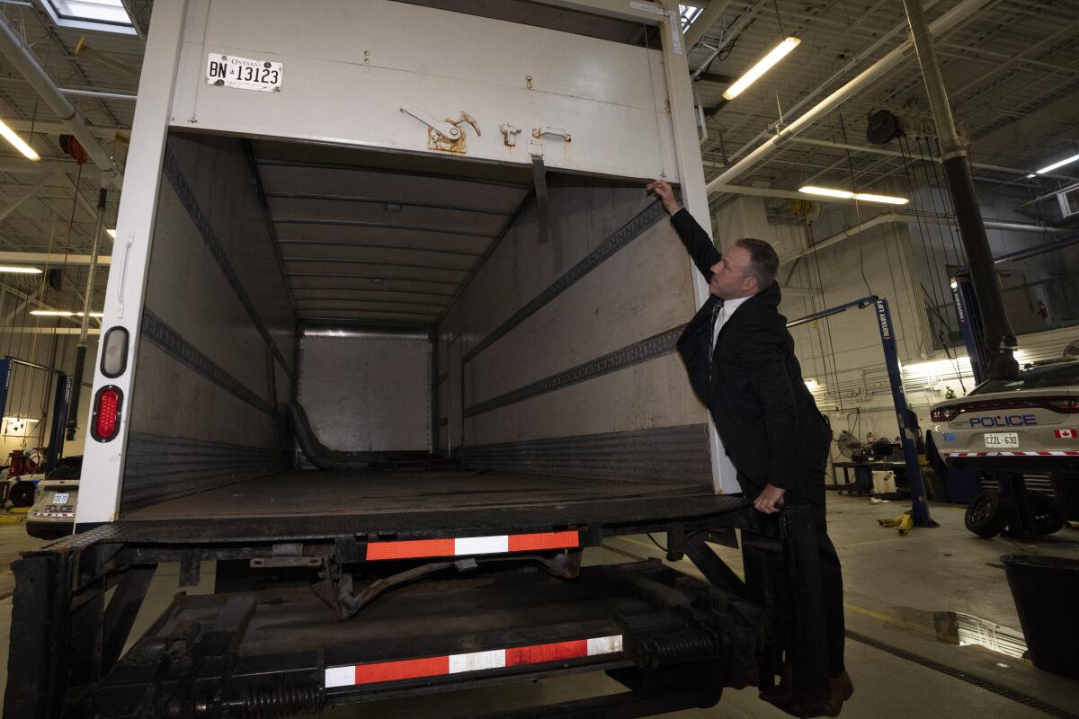 A man in a suit standing on the back of a cargo truck and opening it