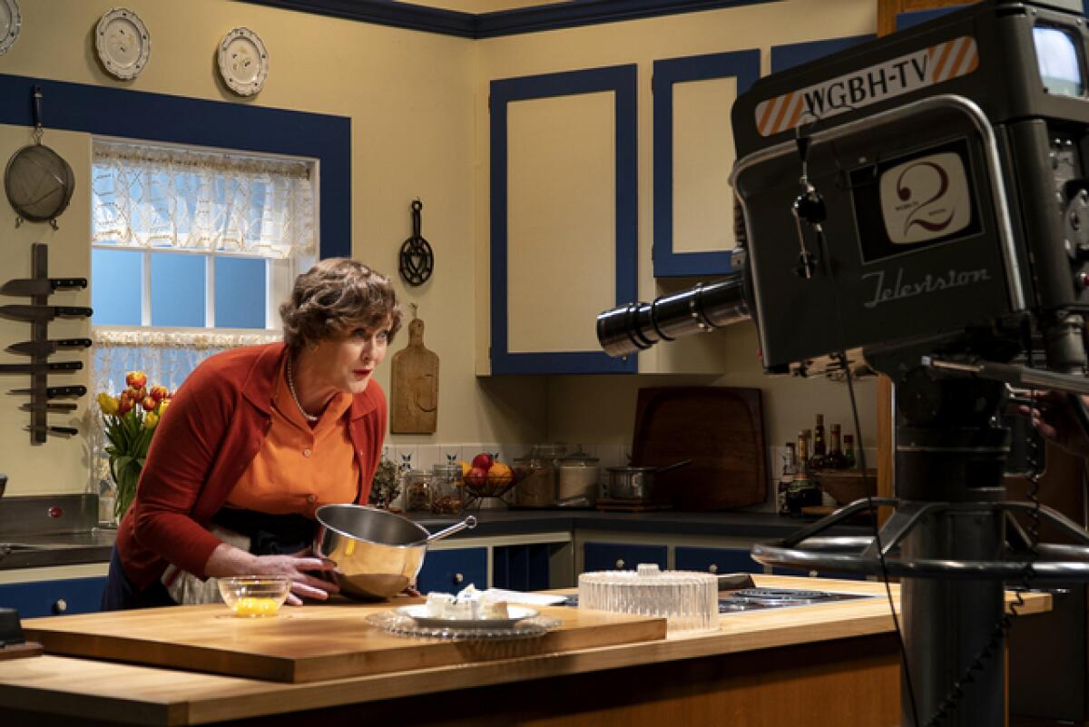 A woman displays a bowl for a TV camera on a cooking show set in the 1950s