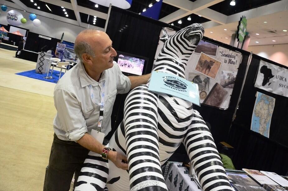 Alan Feldstein of Infinite Safari Adventures grapples with his company's zebra mascot at the Los Angeles Times Travel Show.