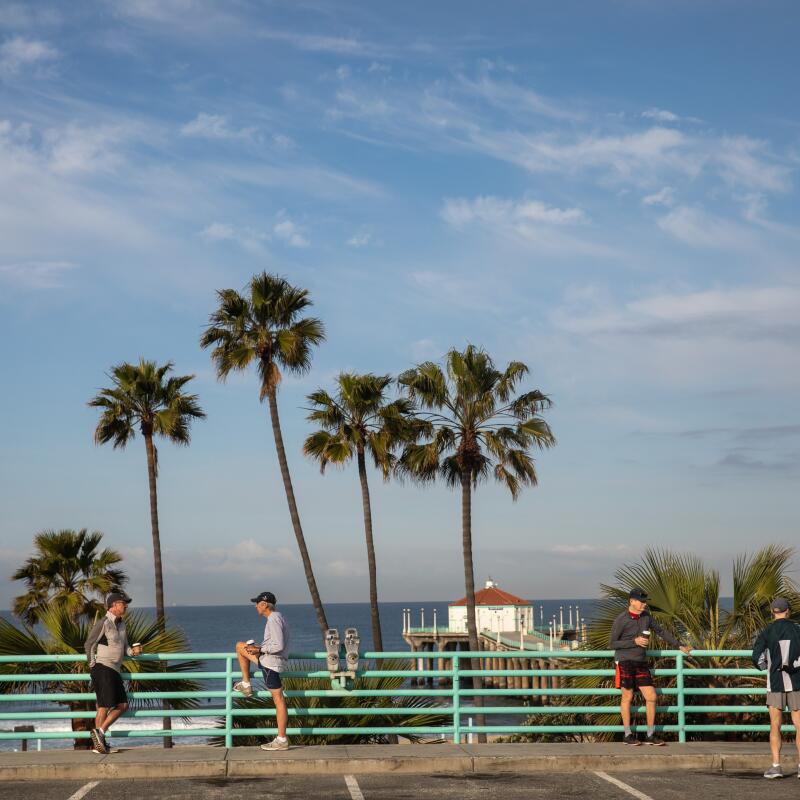 Runners finish their morning with coffee in front of fence, palm trees and beach.