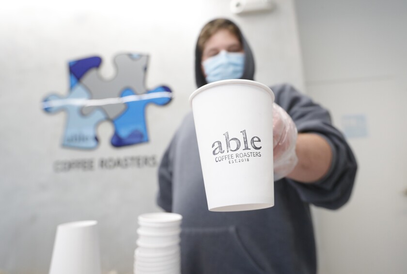 An Able Coffee employee stamps the company logo on coffee mugs.