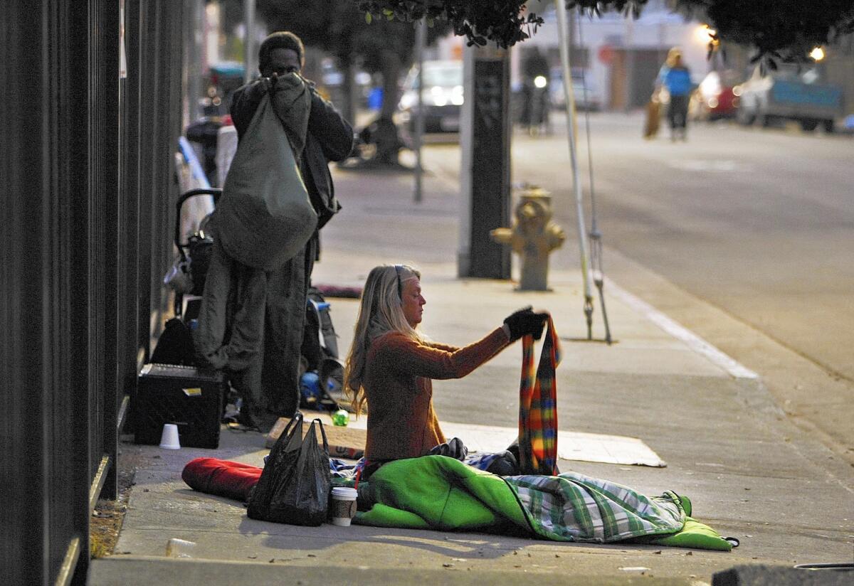 A woman awakened by L.A. police officers on a sidewalk in Venice picks up her belongings.
