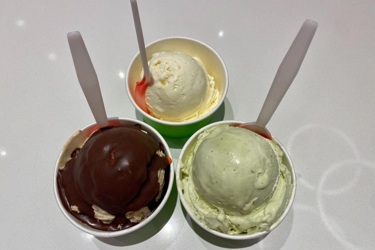 A trio of ice creams in cups with a spoon sticking out of each