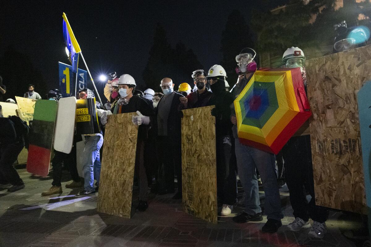 Protesters wear helmets and hold up sheets of plywood.