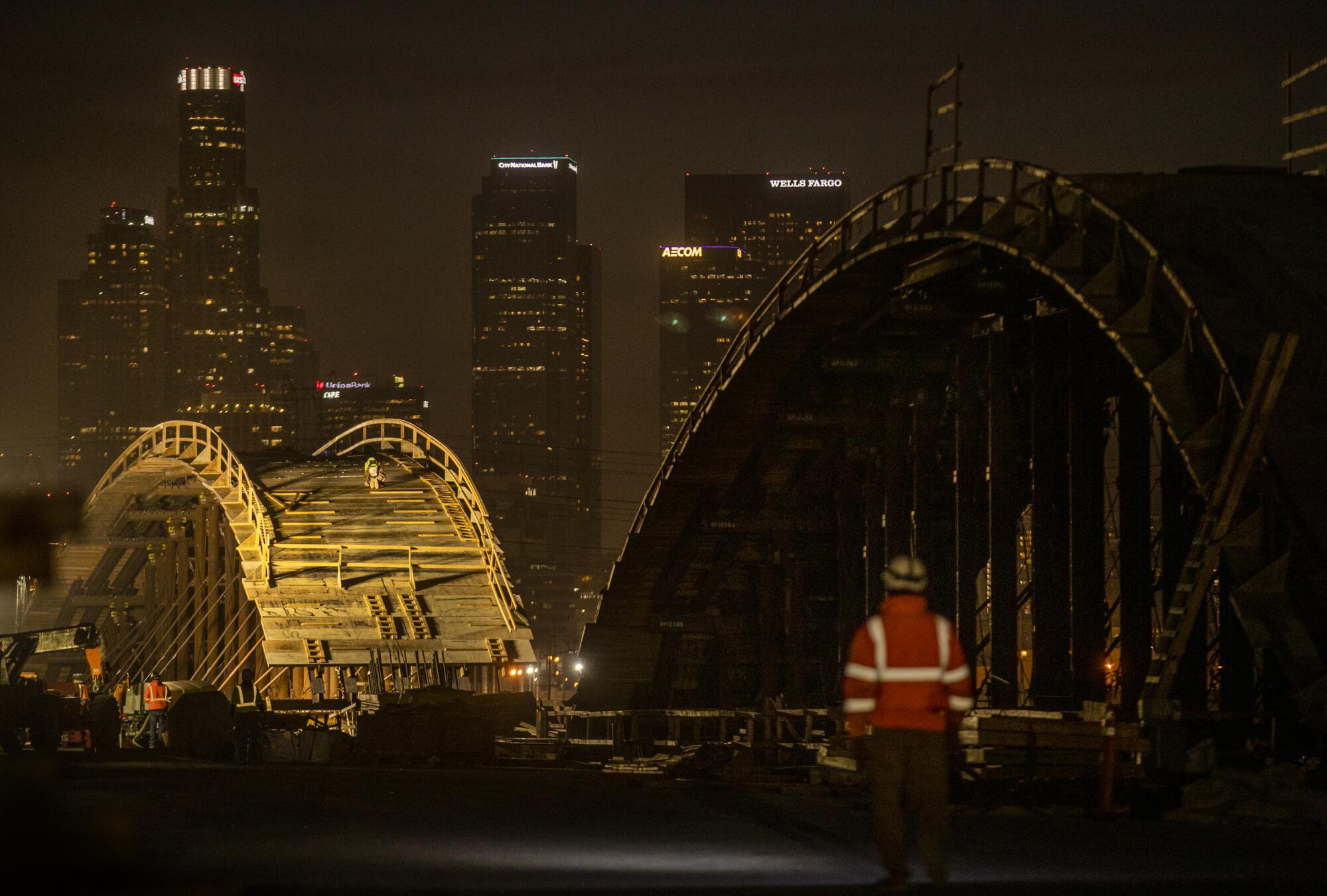 Arches of new bridge in foreground with L.A. high-rises in the distance as night falls 