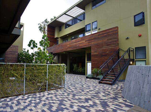 Wider view from inside the courtyard. Stairs lead to a second-floor unit with an expansive deck connected to its apartment by multiple sets of glass doors.