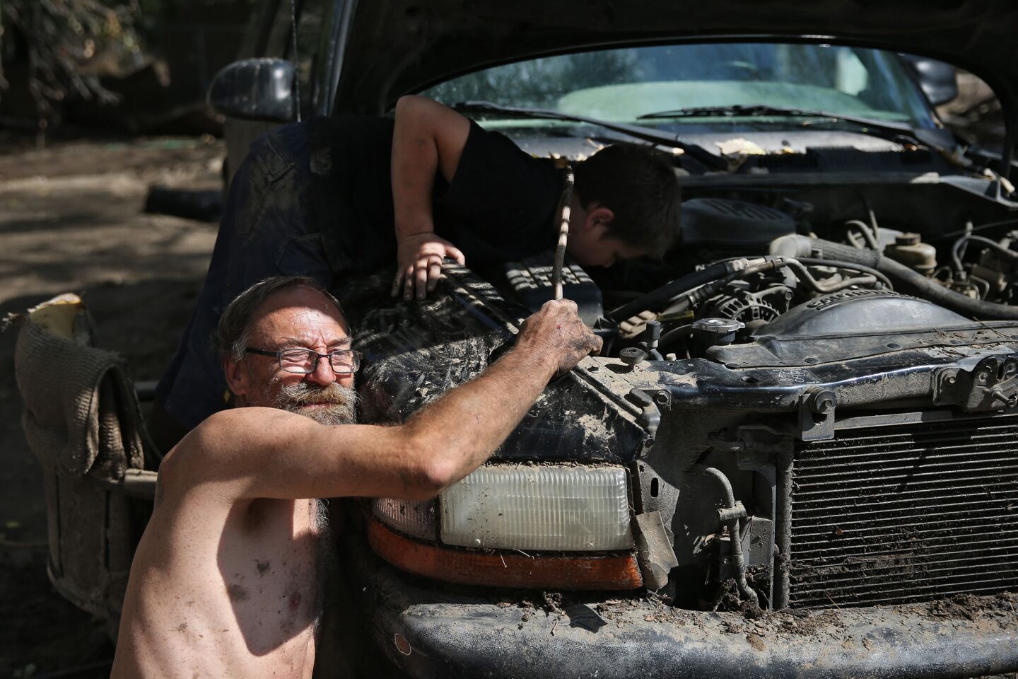 Randy Eisenbeiss of Lake Hughes works on his mud-encrusted SUV with the help of his neighbor, Gian Guadagno, 10.