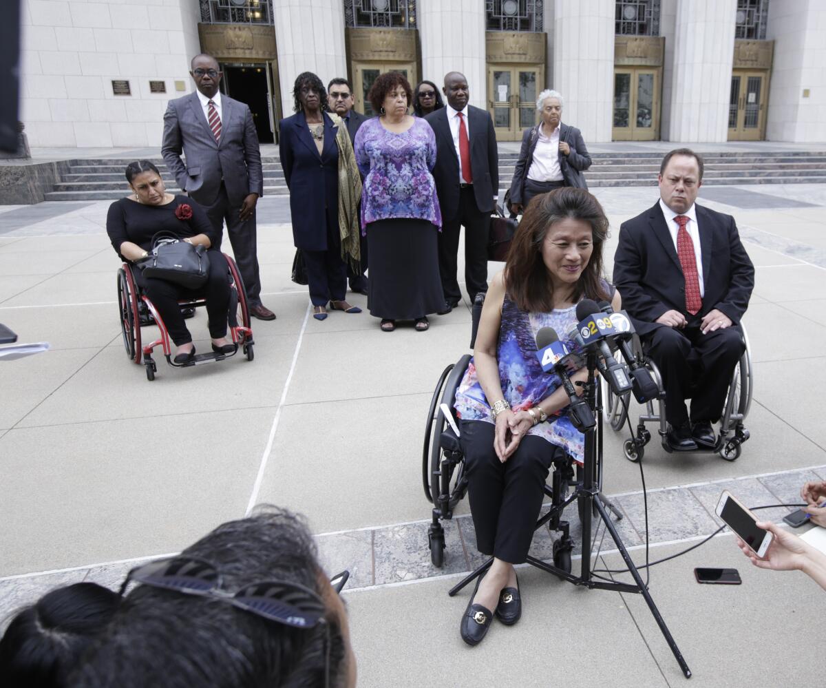 A woman in a wheelchair in front of a group of people speaks outside a courthouse