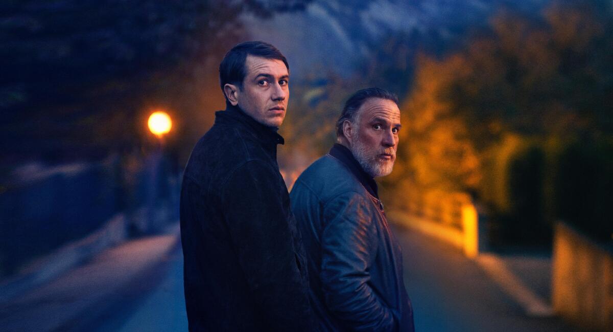 two men look behind them as they walk on a streetlight-lit street 