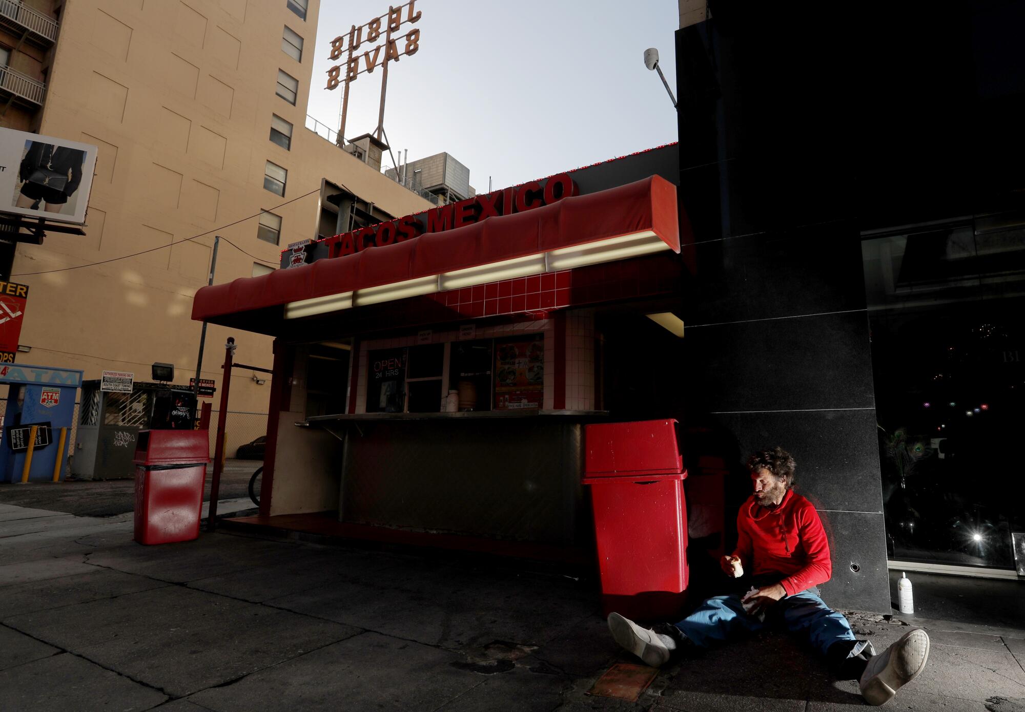 A homeless man named MIke eats food fished from a trash can at a taco stand along Broadway in downtown Los Angeles