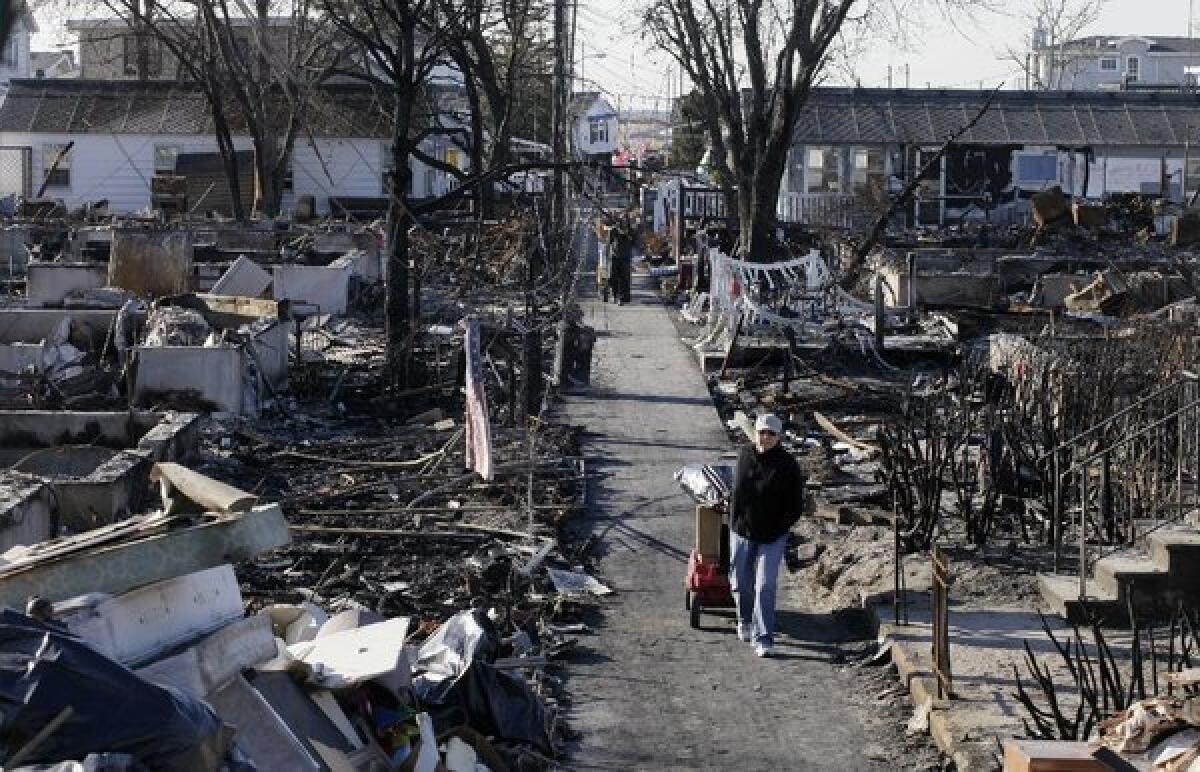 Louise McCarthy carts belongings from her flood-damaged home as she passes charred ruins in the Breezy Point section of New York's Queens borough.