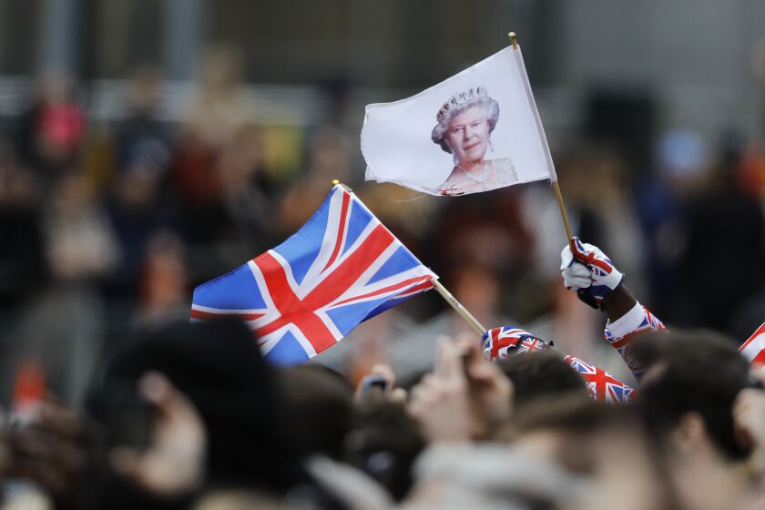 FILE - A man waves a British union flag and a flag bearing the image of Britain's Queen Elizabeth II ahead of the annual Commonwealth Day service at Westminster Abbey in London, Monday, March 9, 2020. After seven decades on the throne, Queen Elizabeth II is widely viewed in the U.K. as a rock in turbulent times. But in Britain’s former colonies, many see her as an anchor to an imperial past whose damage still lingers. (AP Photo/Frank Augstein, File)