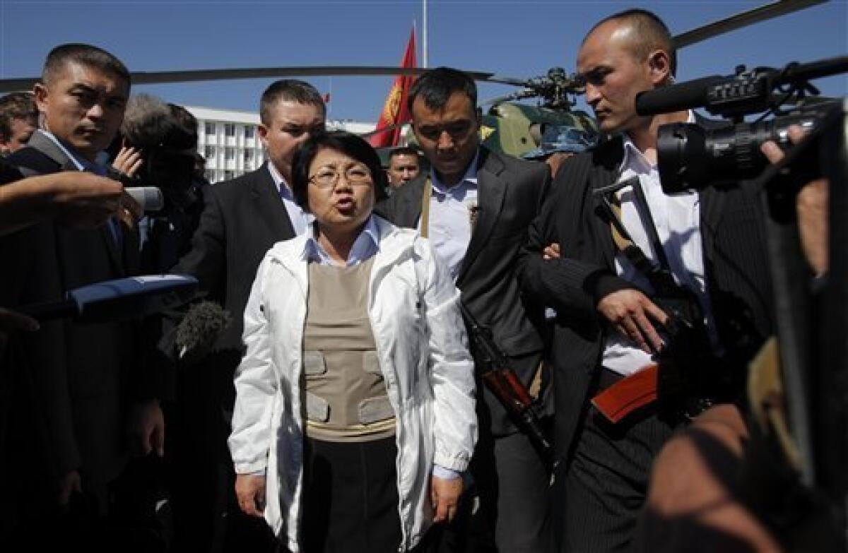 Kyrgyzstan's interim government leader Rosa Otunbayeva, center, wearing a flak jacket, waves after landing by military helicopter on the central square in the southern Kyrgyz city of Osh, Kyrgyzstan, Friday, June 18, 2010. She is vowing to work for the return of refugees who fled deadly ethnic violence there by the hundreds of thousands. (AP Photo/Alexander Zemlianichenko)