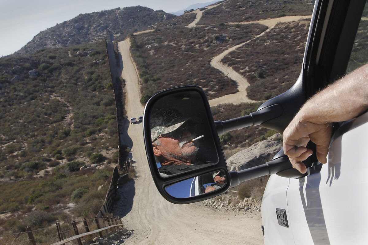 Robert Crooks, reflected in his pickup truck's mirror, is one of several people who patrol the U.S.-Mexico border, left, near Campo, Calif.