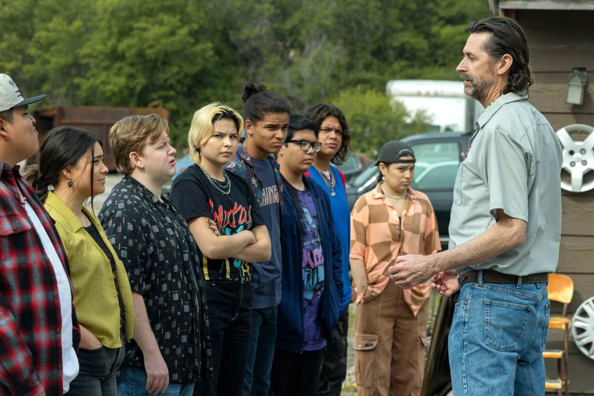 A group of teens standing in a row before a tall older man.