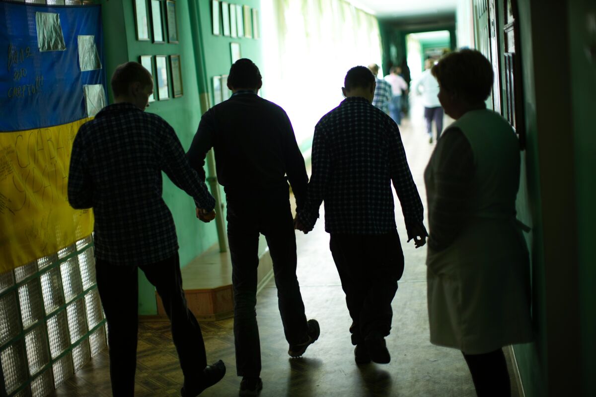 Residents walk along a corridor after lunch time in a facility for people with mental and physical disabilities in the village of Tavriiske, Ukraine, Tuesday, May 10, 2022. The staff is faced with the dilemma of evacuating the facility, and how to do it with minimum disruption to the residents, some of whom have very severe disabilities and others for whom changes in environment can be disorientating and highly stressful. (AP Photo/Francisco Seco)