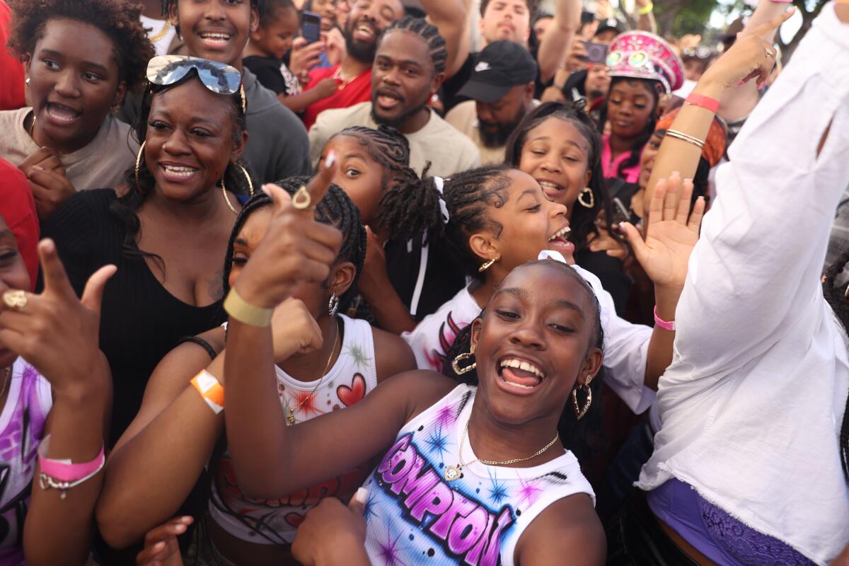 A crowd of young Black women and men smiling and dancing with their hands in the air