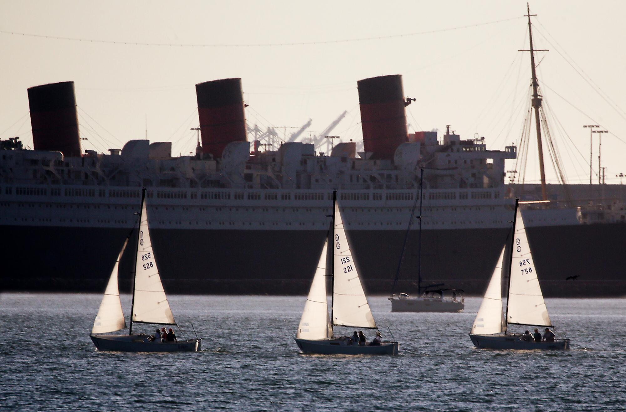 Sailboats race past the Queen Mary as a sea breeze cools the Port of Long Beach.