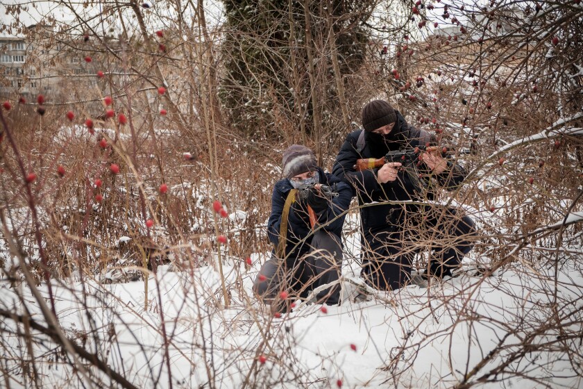 Two people crouched in the snow with guns.