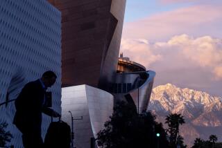 Los Angeles, CA - March 01: A pedestrian crosses the street with a scenic view of The Broad, the Walt Disney Concert Hall and snow-capped San Gabriel mountains at sunset after historic rain and snow dumped on Southern California Wednesday, March 1, 2023 in Los Angeles. (Allen J. Schaben / Los Angeles Times)