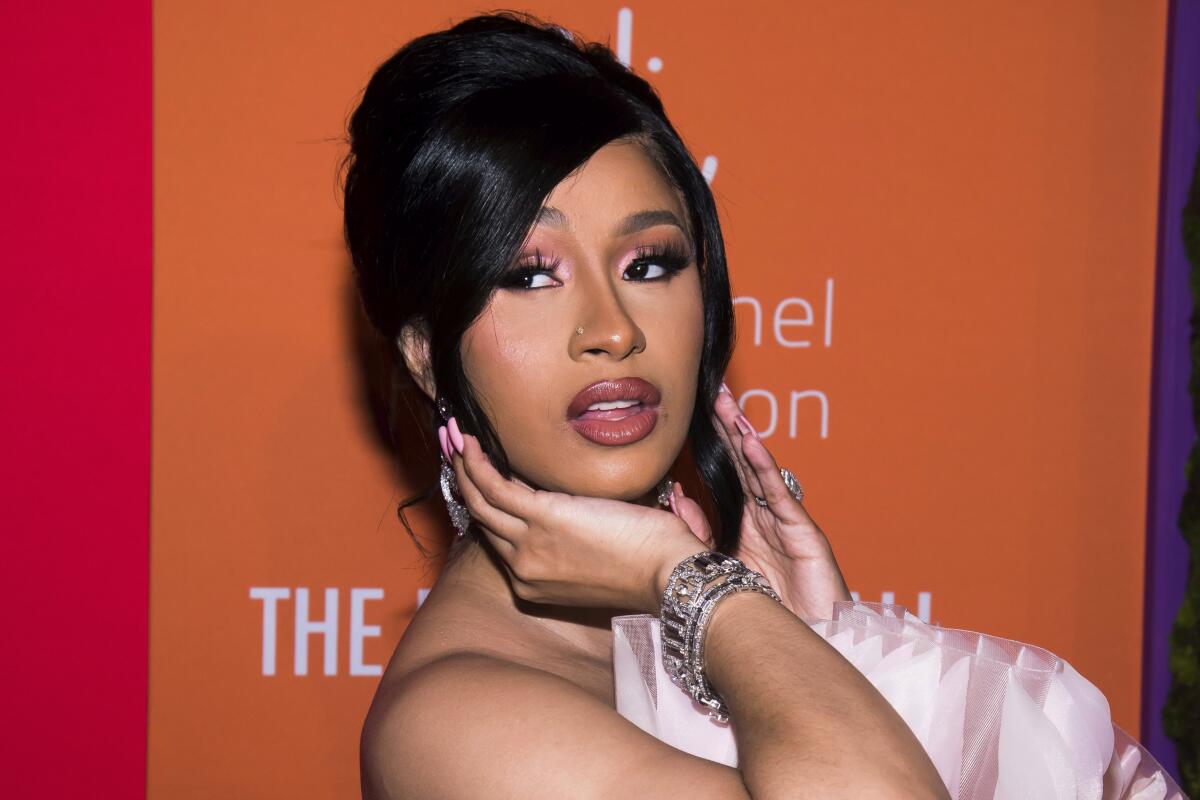 Cardi B looks over her shoulder and cups her face with her right hand