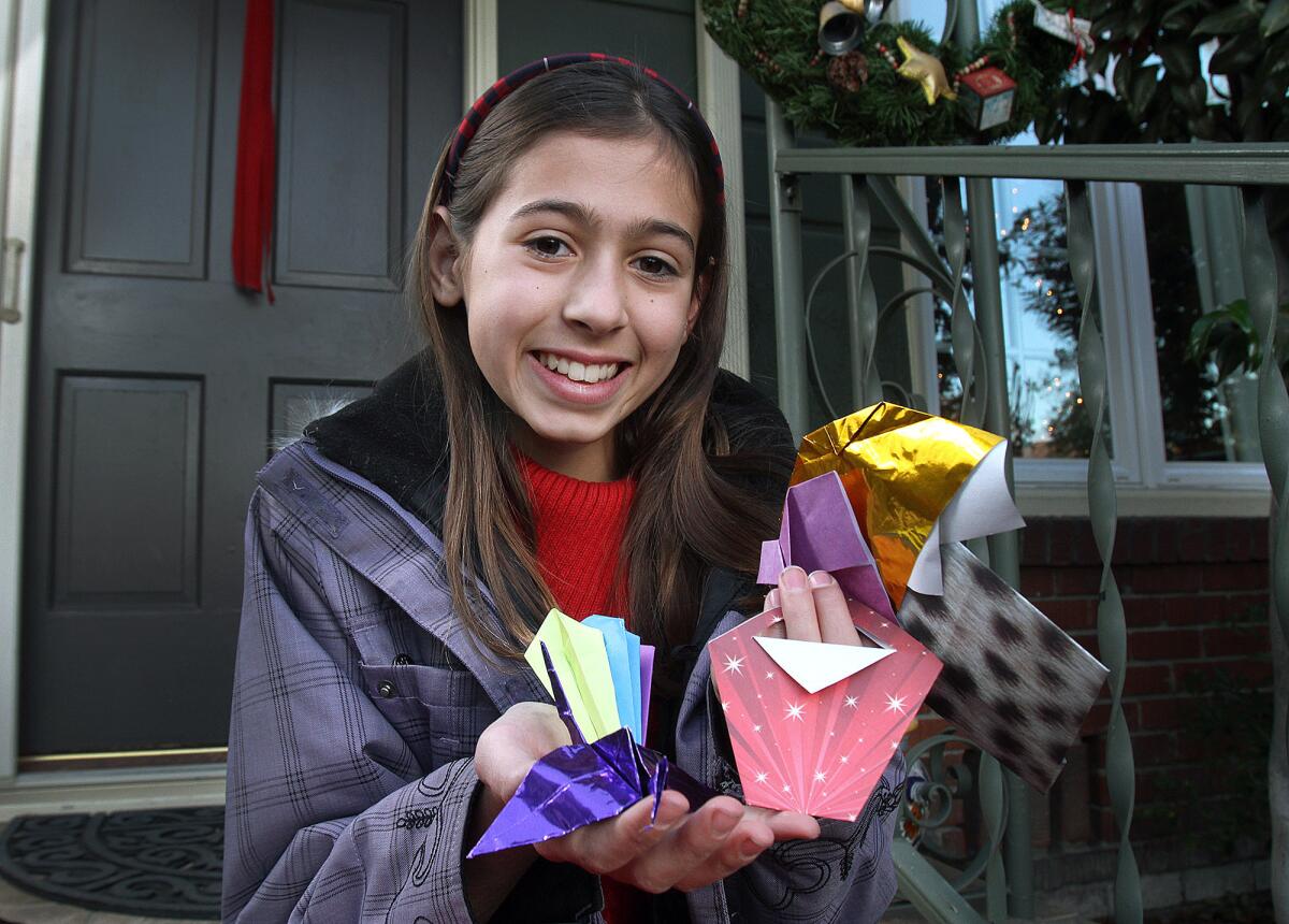Catherine de Wolff, 10, of Burbank holds several of her origami creations on the front step of her family home on Tuesday, Dec. 15, 2015. Catherine has raised more than $1,100 for the Burbank Animal Shelter by working with residents at the Burbank Senior Artists Colony to create origami and solicit donations at the Burbank Farmers' Market.